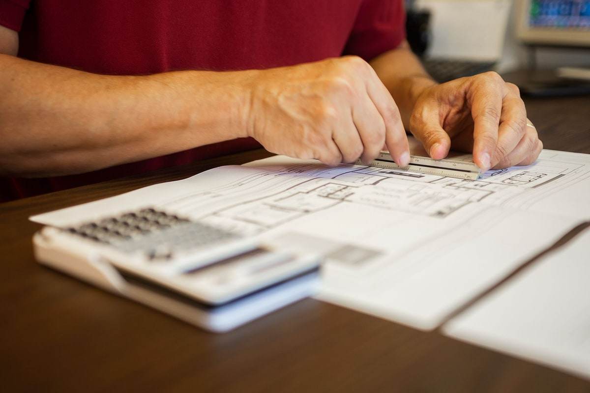 Close view of hands using a ruler over a plan beside a calculator in a staged stock photograph.