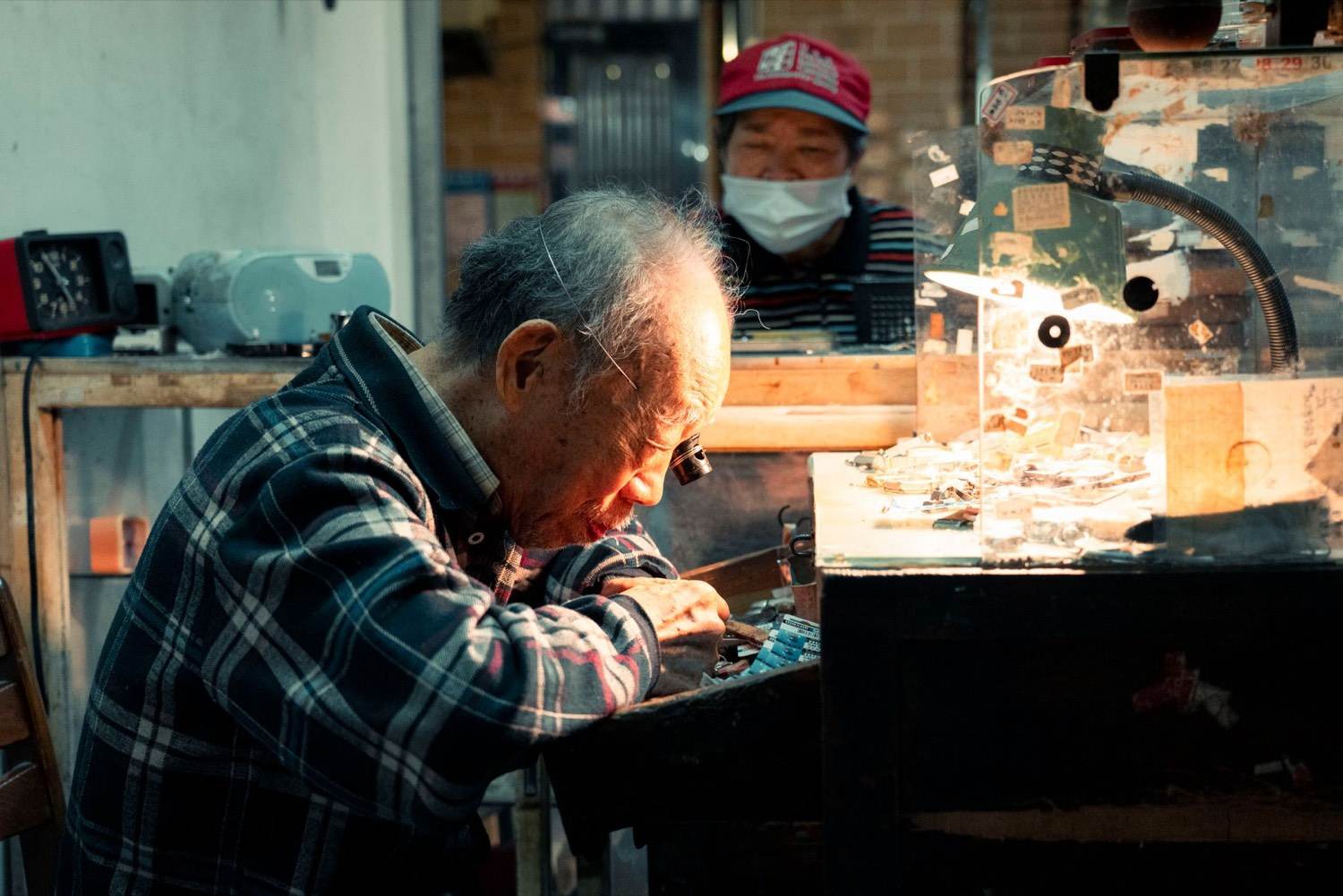 An experienced watchmaker works carefully at a repair bench inside a long-running workshop.