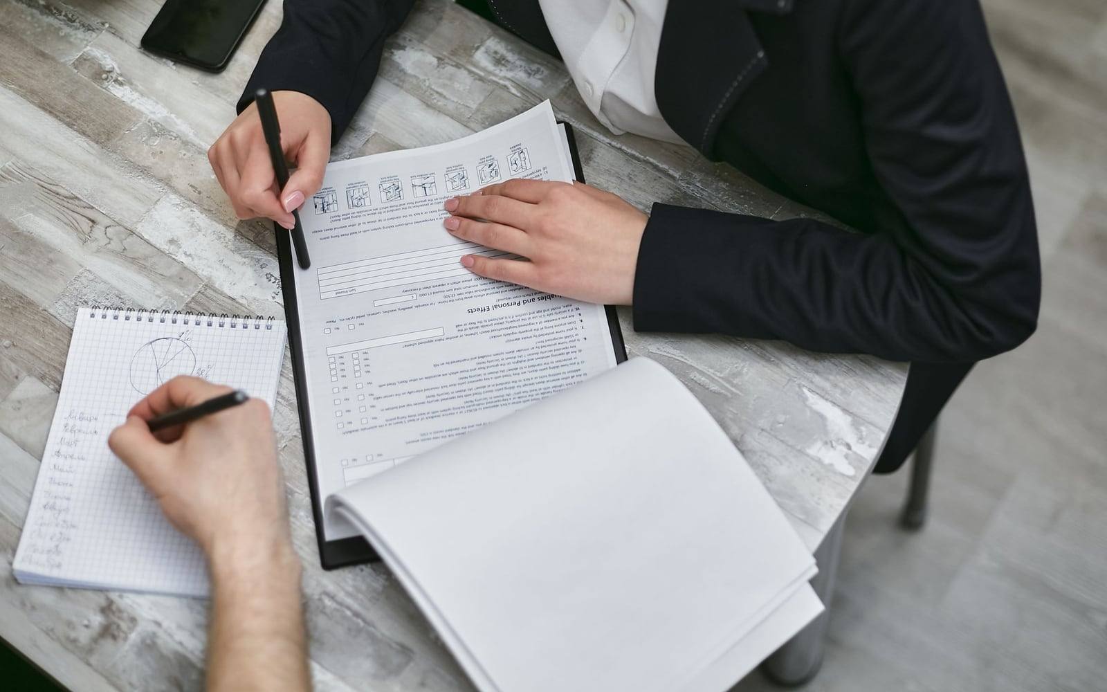 Two people review papers and take notes at a desk in a staged Pexels business photograph.