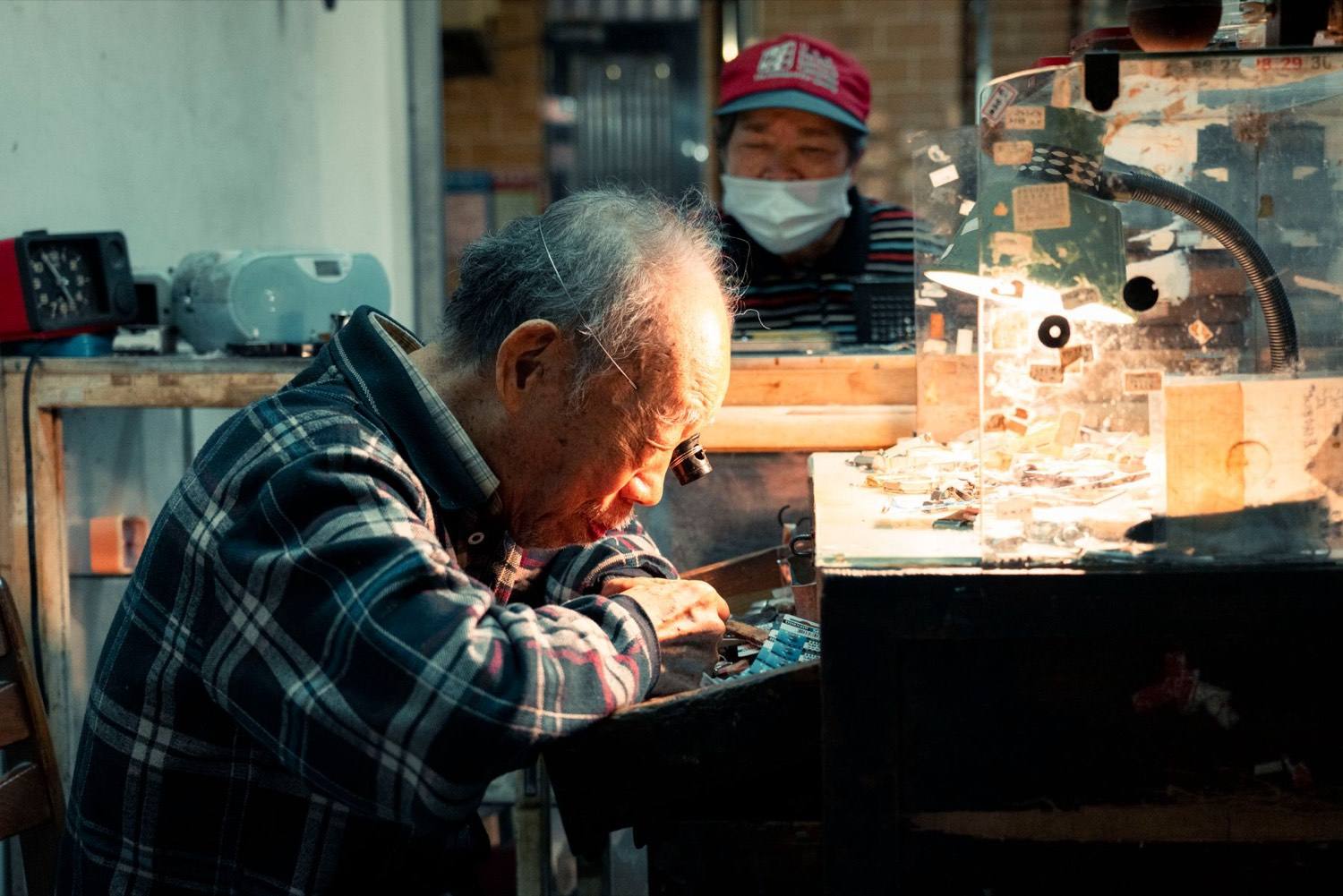 An experienced watchmaker works carefully at a repair bench inside a long-running workshop.